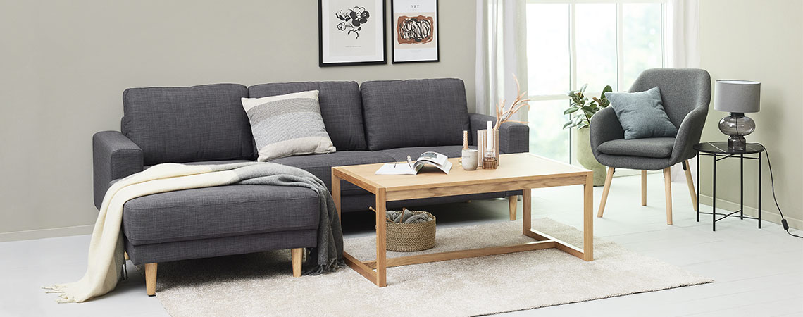 Sufragerie cu canapea gri, măsuță de cafea, fotoliu și un covor pufos pe podea