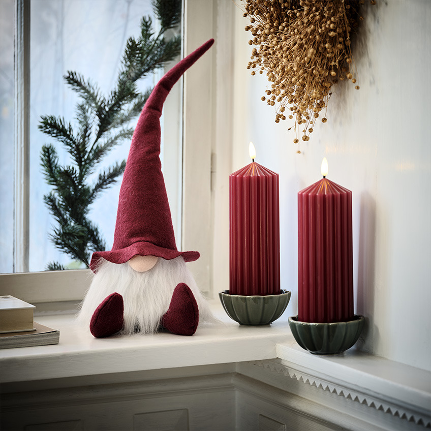 Elf de Crăciun scandinav pe pervaz lângă lumânări mari, roșii