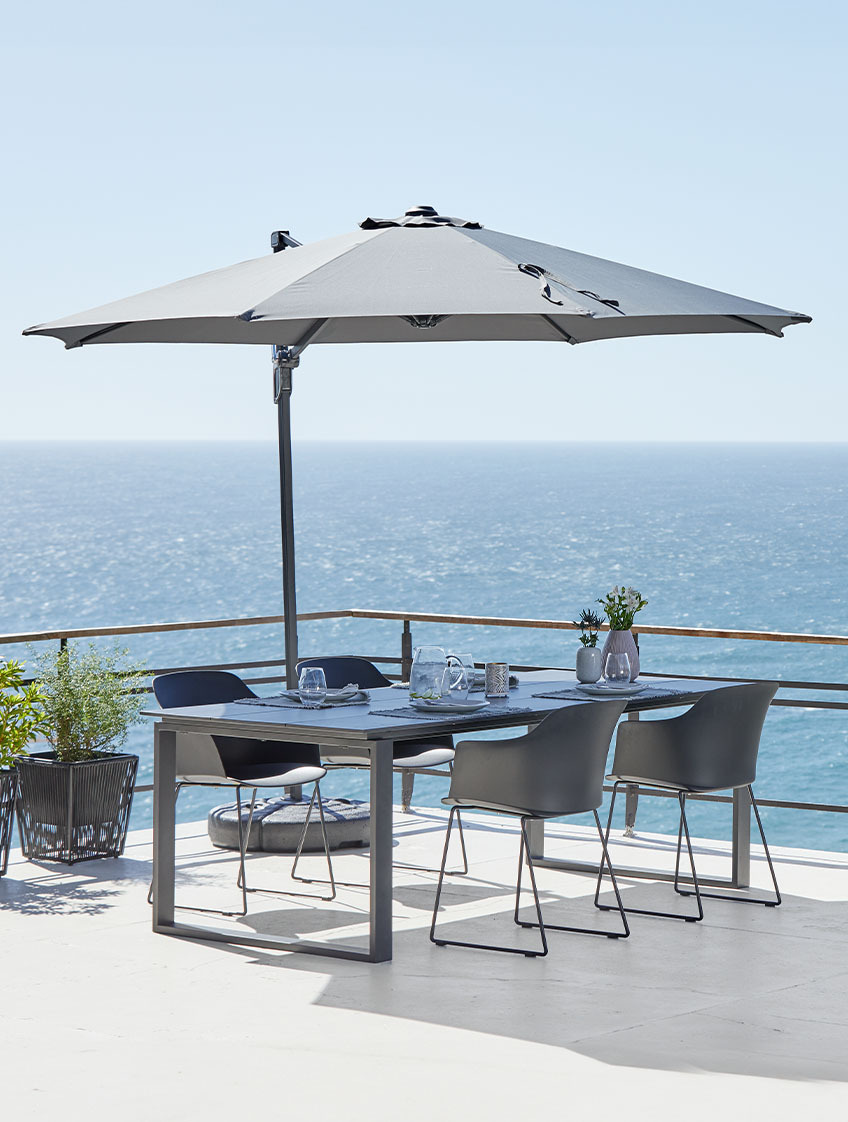 Umbrelă de soare suspendată și masă și scaune de grădină pe terasa de lângă ocean