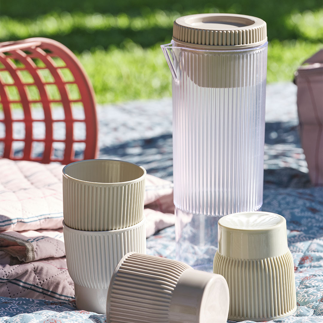 Carafă de picnic TJIM cu patru cești asortate Articole esențiale pentru picnic, inclusiv o carafă cu patru căni asortate pe o pătură de picnic