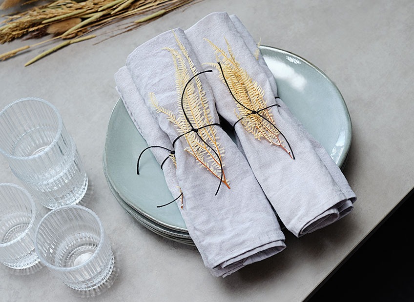 Table set with plate, glasses and cloth napkins decorated with dried leaves and a ribbon 