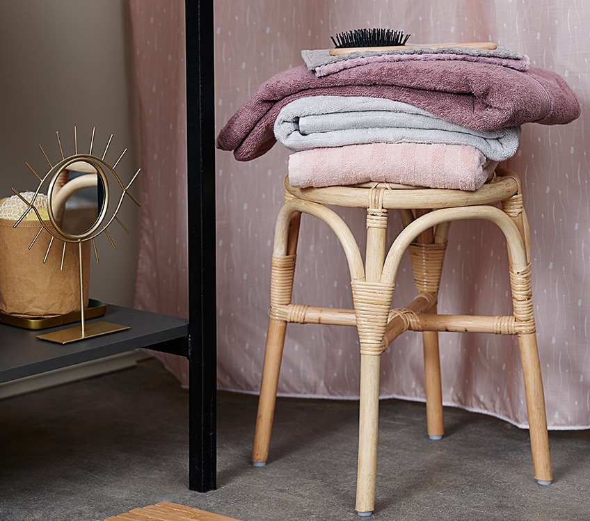 Towels stacked on a stool next to a decorative mirror 