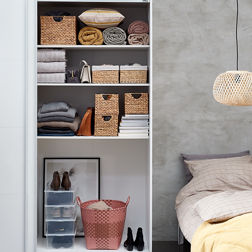 Bedroom with a tidy looking open wardrobe with baskets, stacks of towels and bags