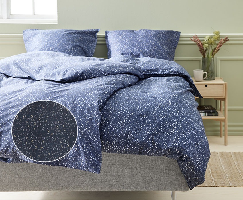 Pat cu lenjerie de pat albastră cu imprimeu într-un dormitor cu noptieră și veioză