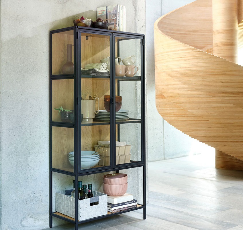 Display cabinet with plates, mugs, bowls and storage boxes by a sculptural staircase 