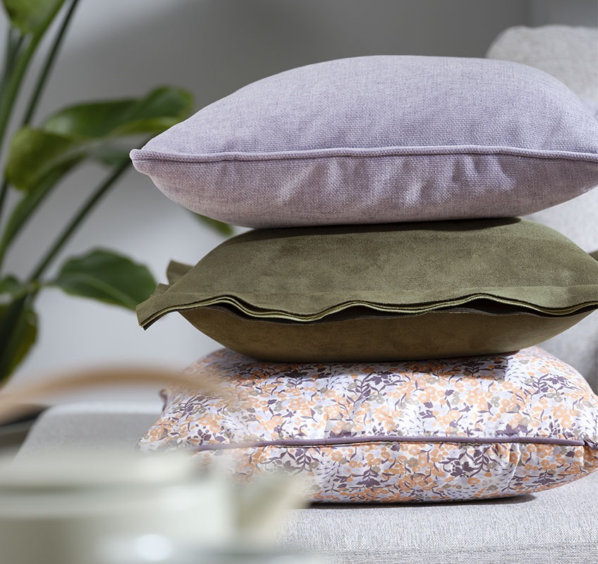 Stack with three cushions: one purple, one green and one with floral print 