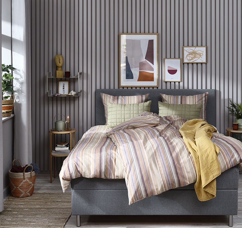 ABBIE bedlinen, VALMUE yellow quilted blanket and green VALMUE cushion A bedroom styled with striped bedlinen, yellow bed throw and green cushions
