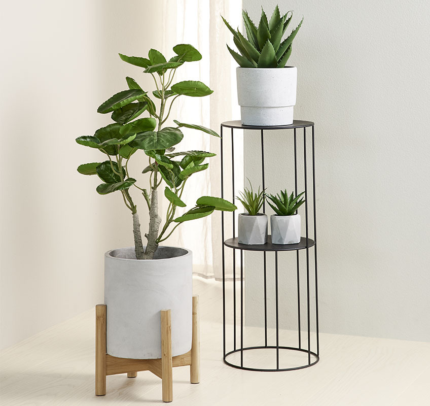 Three green artificial plants in grey planters and in different sizes and shapes