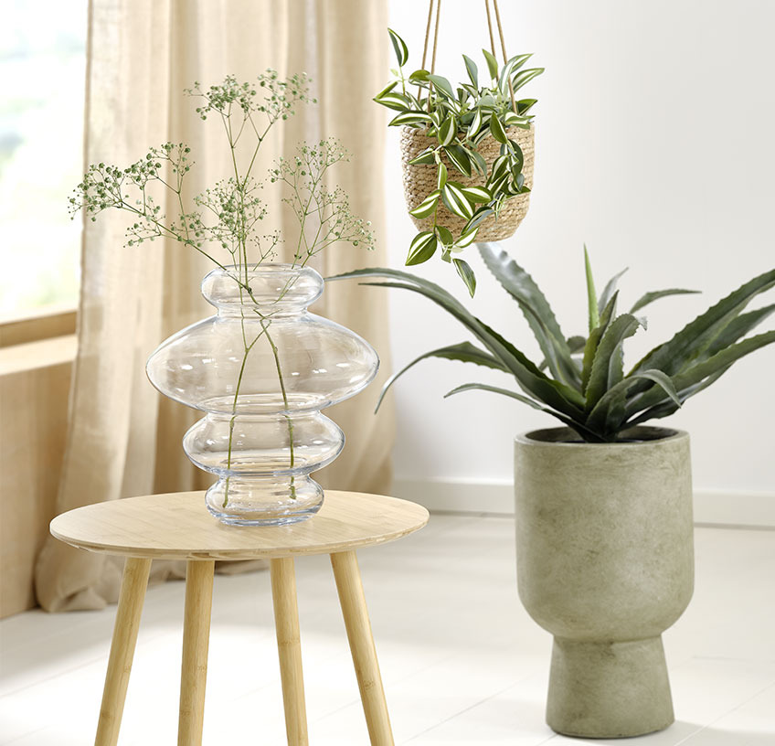 Vază de sticlă pe o masă de colț, ghiveci suspendat și ghiveci cu plante artificiale