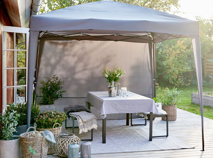 JERUP gazebo Grey gazebo with a decorated and set table and benches on patio